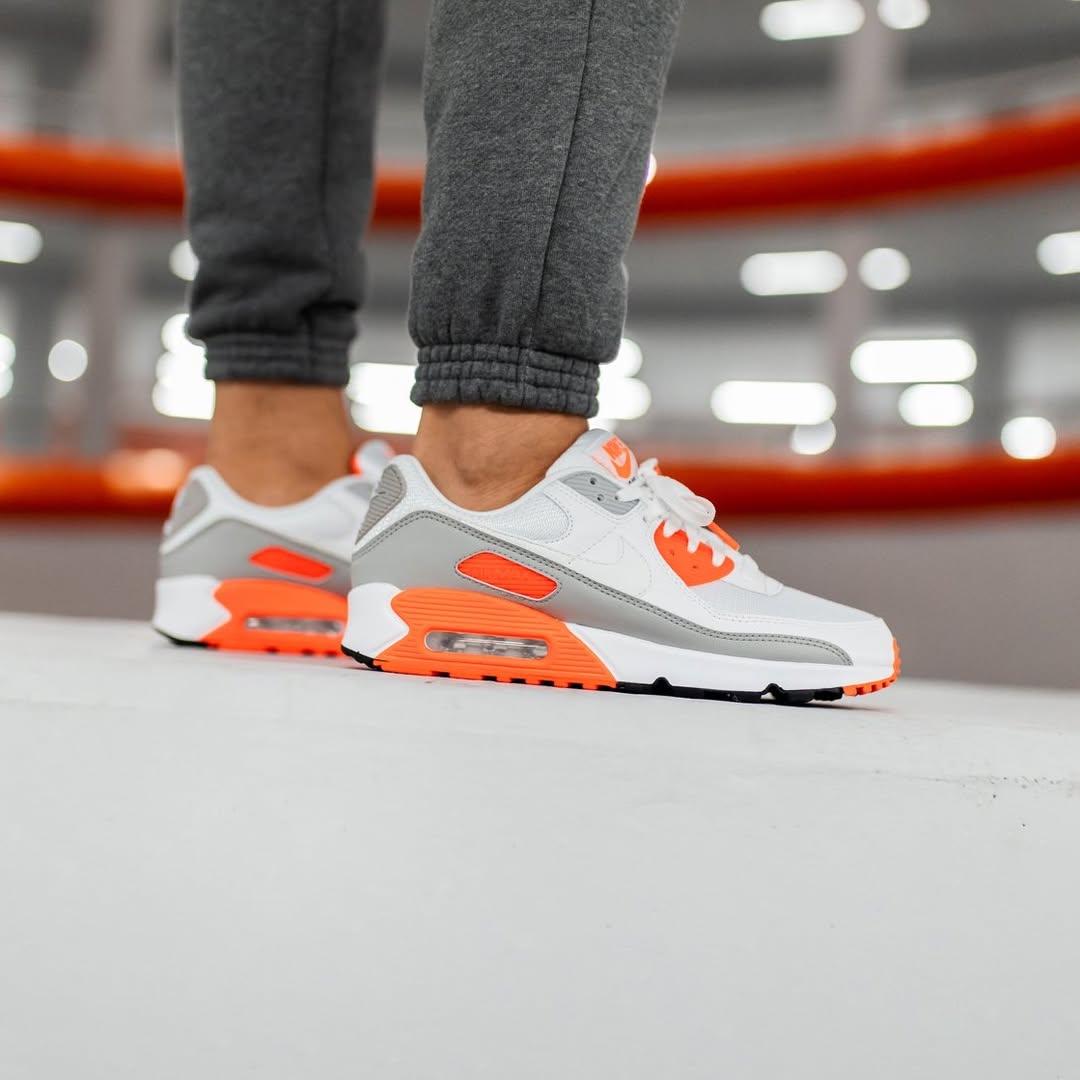 Achteraanzicht van de sneaker met zicht op zwart-oranje Nike Air-logo, grijze overlays en witte midsole – strak kleurcontrast met OG-feel