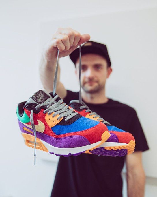 In hand shot van de Air Max 90 Red met zicht op textuur van rood suède en gele Swoosh – rijke materialen en krachtige contrasten