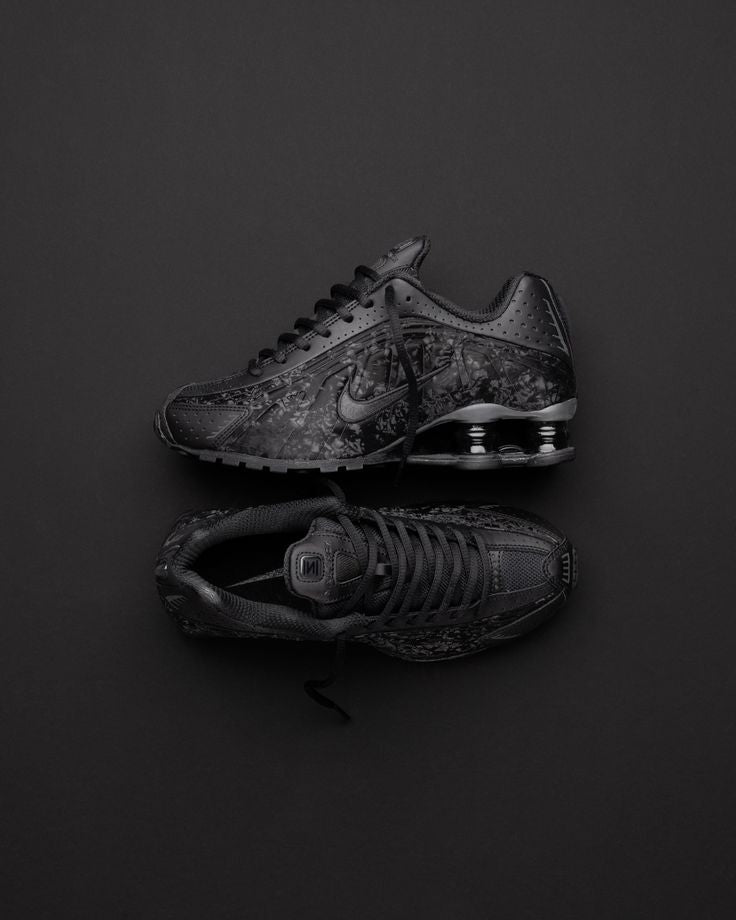 Nike Shox R4 Black Floral op donkere achtergrond, waarbij de floral textuur en reflectie van de zool contrasteren met het licht