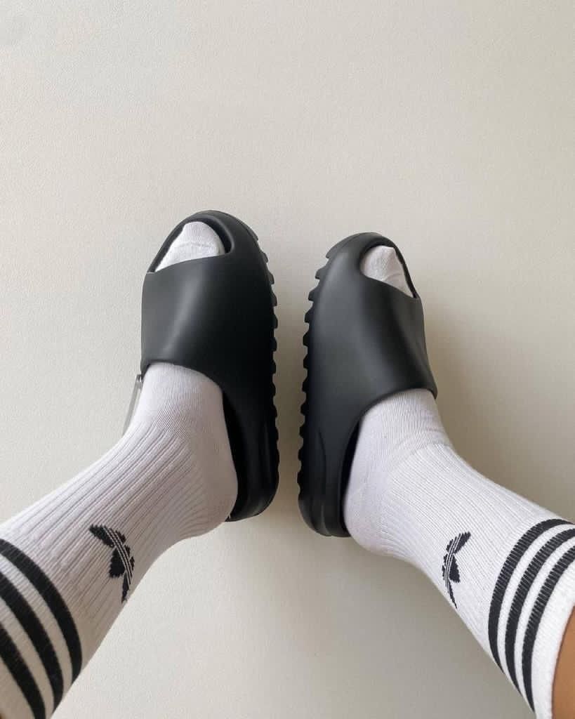 Yeezy Slide Granite ID4134 aan voet met witte adidas sokken – donkere en rustige streetwear fit voor zomer of airport look