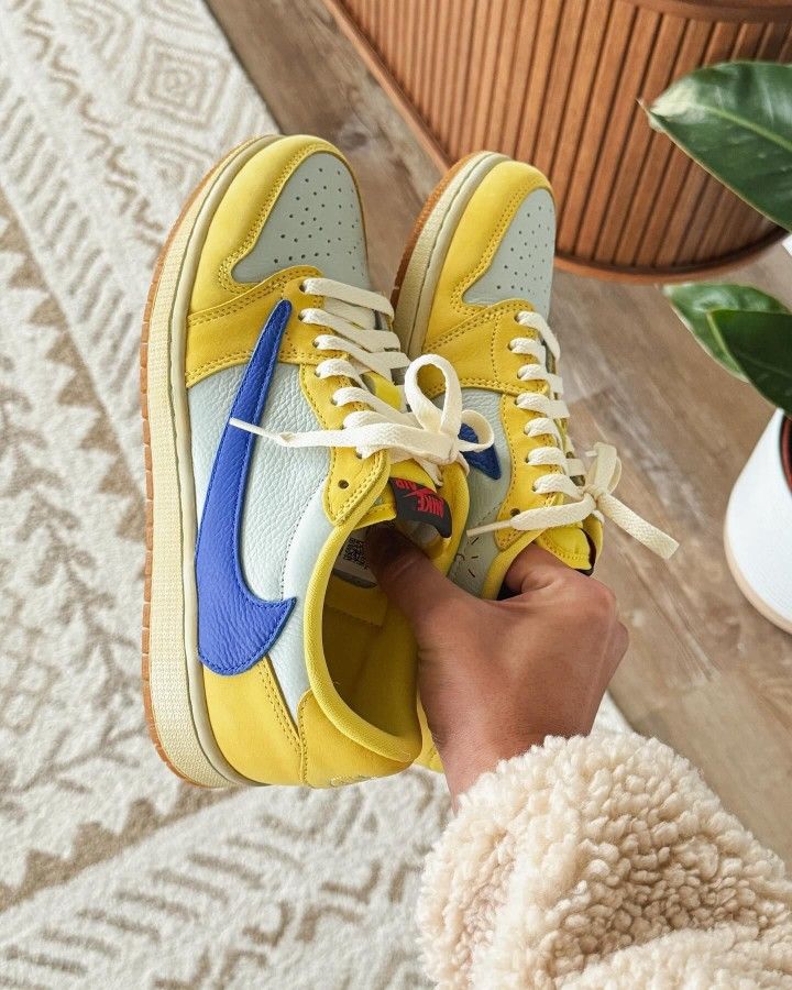 Air Jordan 1 Low OG Travis Scott Canary (SKU DZ4137‑700) – in‑hand shot met zicht op reversed Swoosh, gum outsole en Racer Blue accents