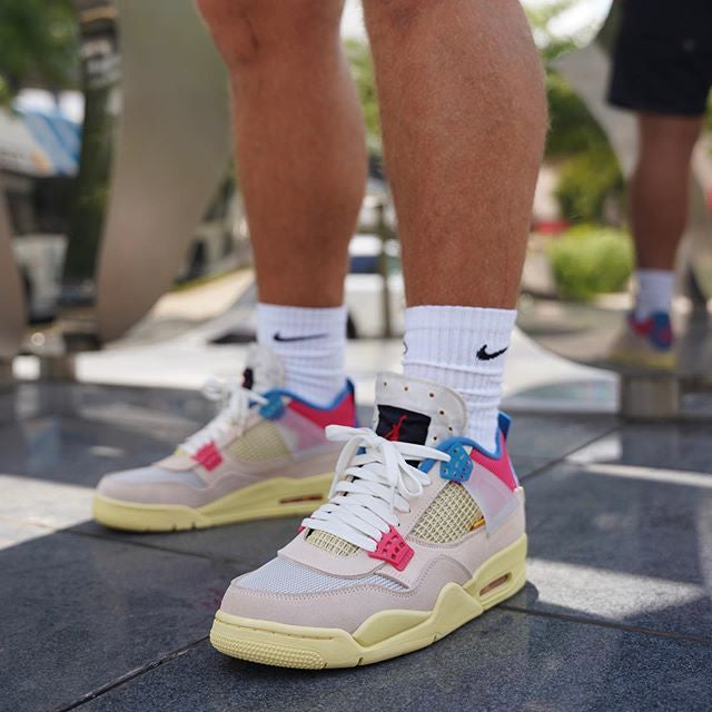 Guava Ice DC9533-800 gedragen op straat met loose-fit broek en witte sokken, felblauwe veters en rode branding zichtbaar tijdens het lopen