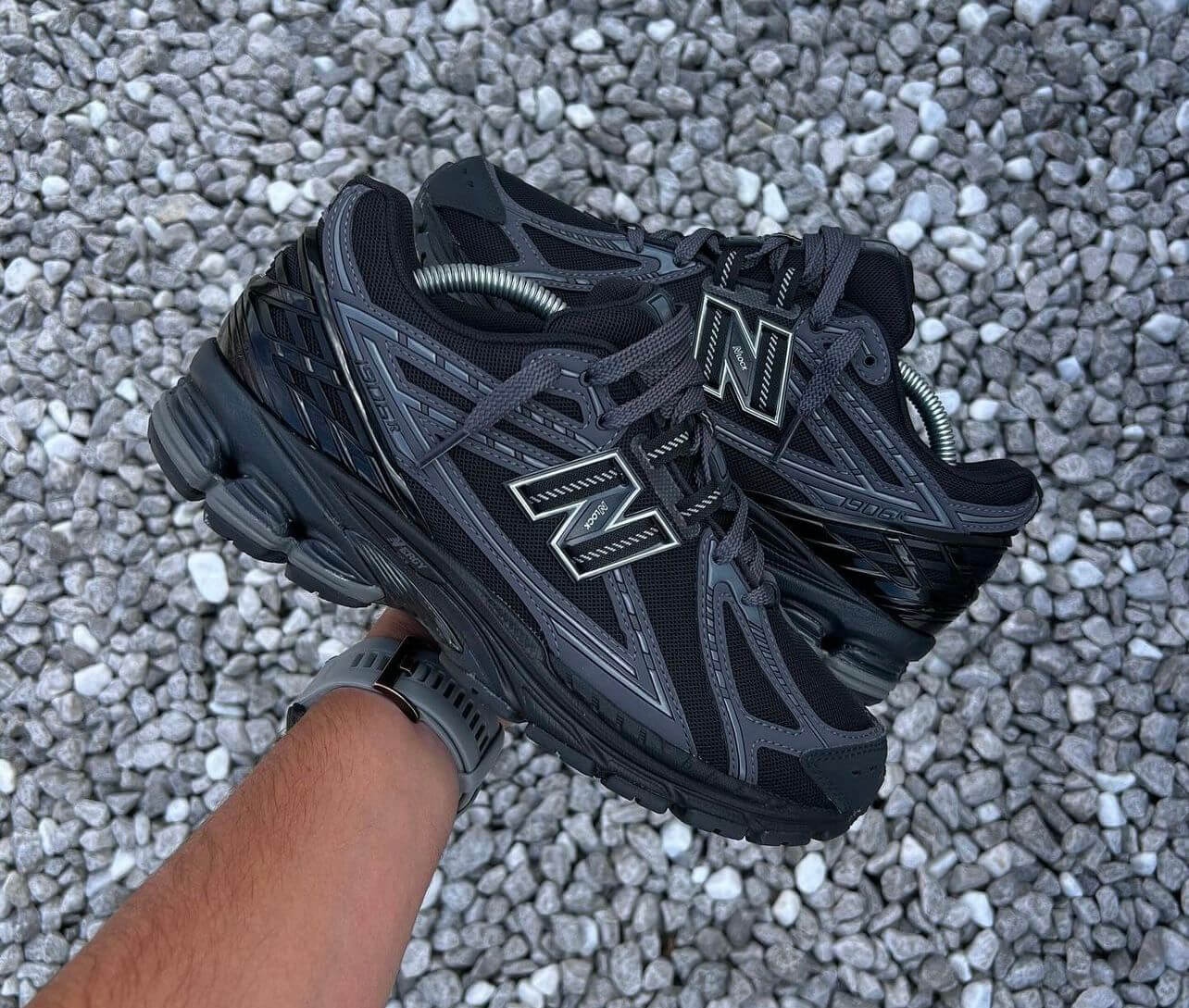 Close-up van het bovenwerk van de 1906R Black Phantom met ademend mesh, matte overlays en tonale details. De textuur geeft deze triple black sneaker diepte en karakter.