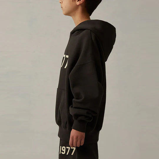Fear of God Essentials 1977 Hoodie Iron on body – gedragen met tonale of zwarte fit, relaxed silhouet en statement frontlogo via Snrkickz