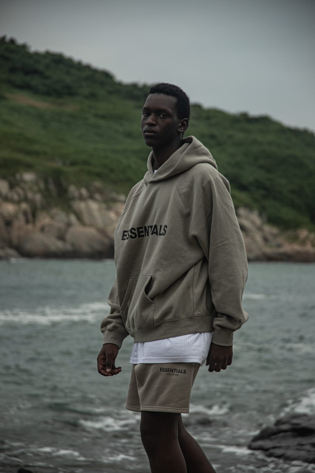 Fear of God Essentials Hoodie Moss – model draagt mosgroene hoodie in stedelijke omgeving met relaxed streetwear look