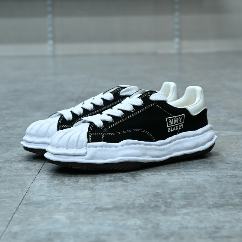 Maison Mihara Yasuhiro Blakey OG Sole Canvas Low Black - Maison Mihara Yasuhiro Blakey OG Sole Canvas Low Black – model draagt Regular fit sneaker met tapered denim voor een avant-garde streetwear look