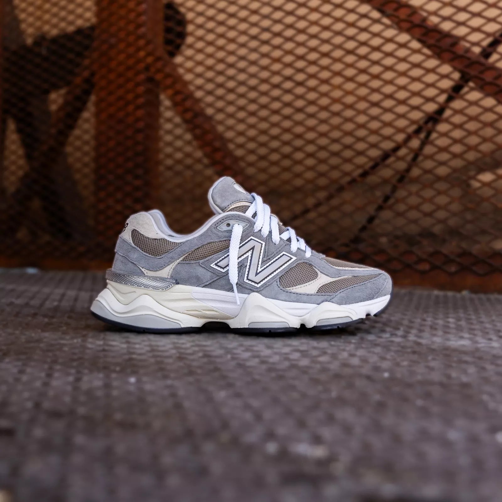 New Balance 9060 Slate Grey met Arid Stone details gestyled in industriële setting met mesh-achtergrond
