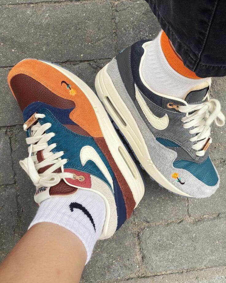 In-hand shot van Nike Air Max 1 Kasina Won-Ang Orange DQ8475-800 – textuur van suède en details zoals het Won-Ang logo en reflectieve elementen