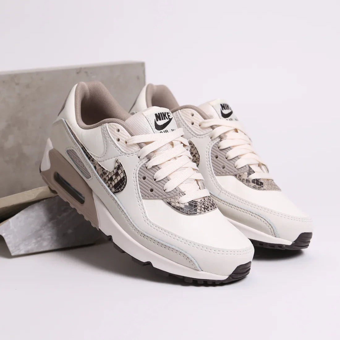 In hand shot van de Nike AM90 Light Pink Snakeskin met zachte materialenmix, beige mesh toebox en roze accenten
