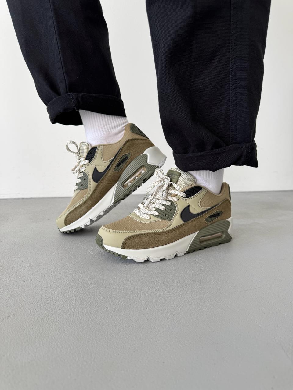 In hand shot van de Nike AM90 Neutral Olive met canvas textuur, suède mudguard en licht crèmekleurige zool