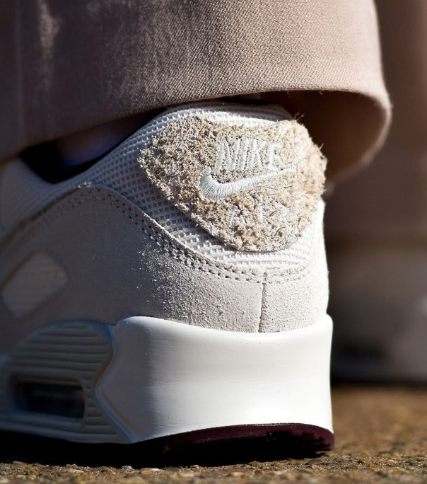 In hand shot van de Nike Air Max 90 Premium in Sail met stevige materialenmix, zichtbare Air-unit en dieprode details