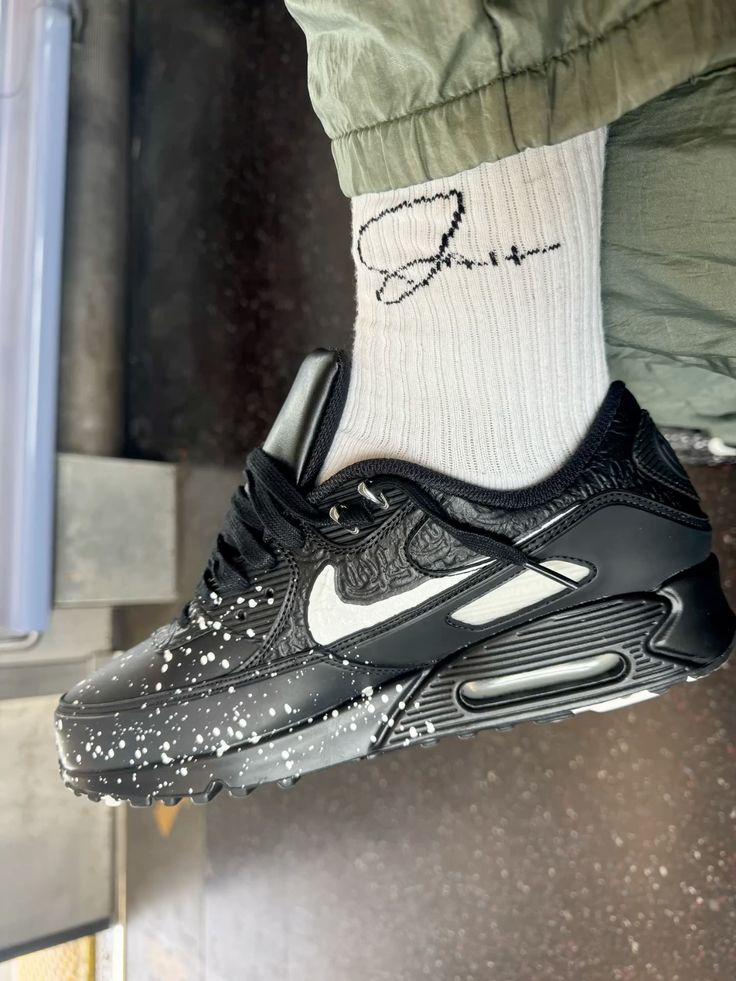 In hand shot van de Nike AM90 Slawn Black met glanzende kunstprint, suède afwerking en zwarte zool