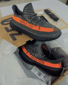 Adidas Yeezy Boost 350 V2 Carbon Beluga HQ7045 vastgehouden boven de originele Yeezy doos, met zicht op knit details en oranje streep