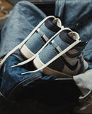 Flatlay van de sneaker naast de bijbehorende rode box – helder contrast tussen denim, wit leer en goudaccenten

