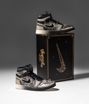 Air Jordan 1 Día De Muertos naast zwarte schoenendoos met gouden accenten – luxe presentatie met thematische illustraties en symboliek