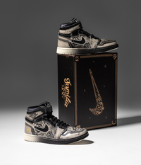 Air Jordan 1 Día De Muertos naast zwarte schoenendoos met gouden accenten – luxe presentatie met thematische illustraties en symboliek