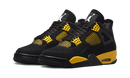 Close-up van de Air Jordan 4 Thunder met zwarte upper, gele veterhouders en stevige zwarte zool met contrastdetails.