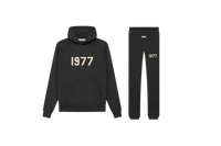 Studiofoto van de Fear of God Essentials IRON 1977 Full Set bestaande uit hoodie en sweatpants in zwarte kleur met 1977 opdruk