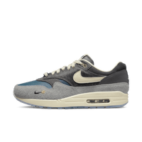 Zijkant van de Nike Air Max 1 Kasina Grey met premium suède, pony hair en zilveren mini Swoosh – Koreaanse collab met diepe materialenmix