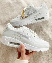 In hand shot van de sneaker met zicht op glanzend wit leer, de Lucky Charms ketting en zichtbare Air-unit – elegant en licht van karakter

