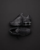 Nike Shox R4 Black Floral op donkere achtergrond, waarbij de floral textuur en reflectie van de zool contrasteren met het licht