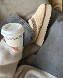 Close-up van UGG Tazz Slipper Heritage Braid Natural 1143976-NAT met zachte woltextuur, gevlochten rode kraag en warme binnenvoering, gefotografeerd in cozy setting door Snrkickz.