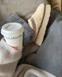 Close-up van UGG Tazz Slipper Heritage Braid Natural 1143976-NAT met zachte woltextuur, gevlochten rode kraag en warme binnenvoering, gefotografeerd in cozy setting door Snrkickz.