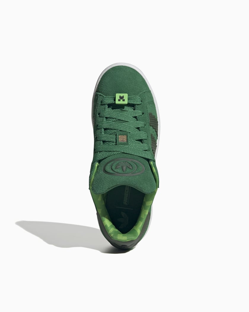 Detail van de Adidas x Minecraft branding op tong en hiel, met pixel graphics en suède textuur via Snrkickz