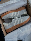 Adidas Handball Spezial Wonder Silver Gum – close-up van de zilvergrijze suède textuur met goudkleurig Spezial-logo en witte leerdetails