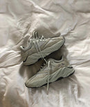 Adidas Yeezy 700 Salt EG7487 gefotografeerd in casual streetwear setting op betonvloer, waarbij de monochrome look en retro lijnen duidelijk uitkomen