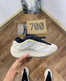 Flatlay van Yeezy Azael naast originele 700-doos, sneaker in hand boven houten vloer met zicht op zool en upper