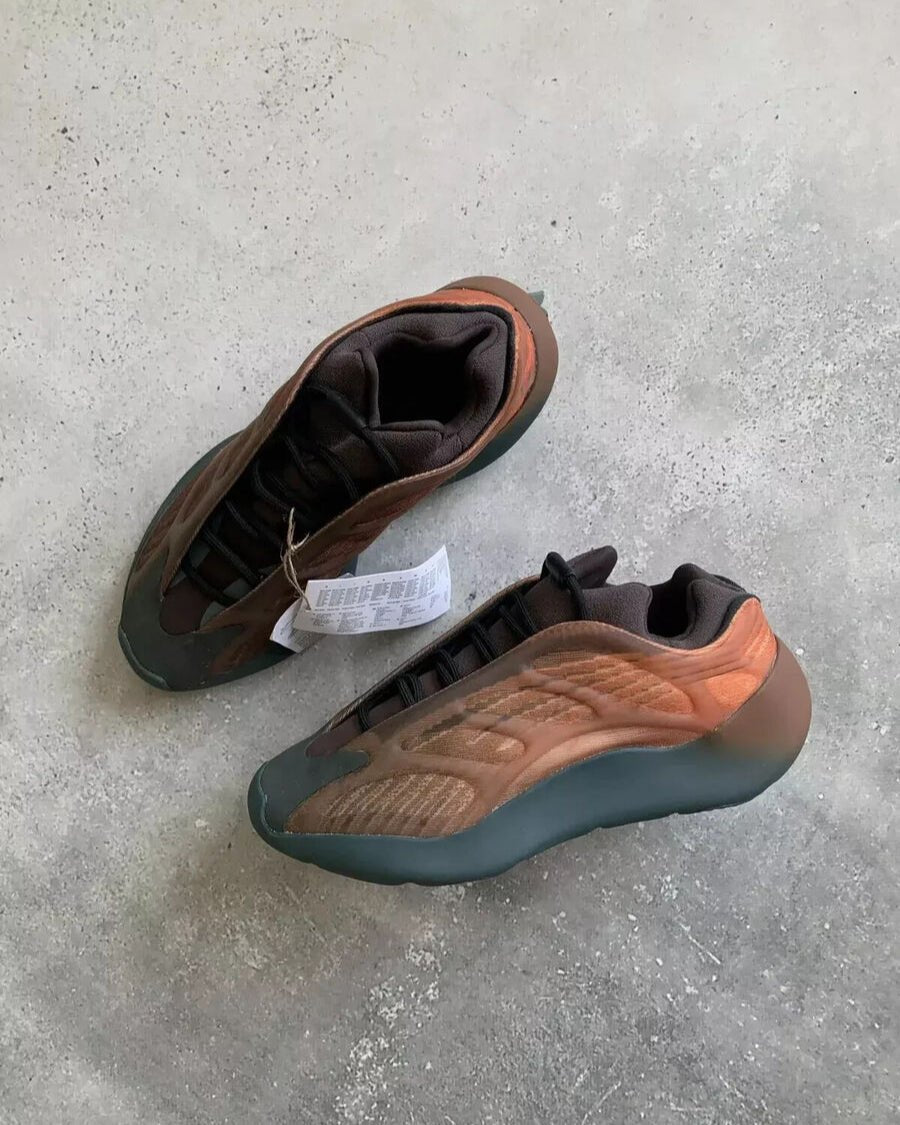 Flatlay van de Yeezy 700 Copper Fade op betonnen vloer met doos en label, highlighting de fade van oranje naar bruin