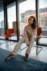 On-foot beeld van vrouw in relaxte pose met de Yeezy 700 V3 Copper Fade, zittend op designstoel in modern interieur