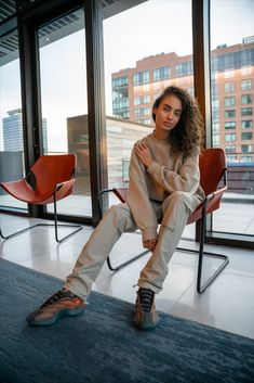 On-foot beeld van vrouw in relaxte pose met de Yeezy 700 V3 Copper Fade, zittend op designstoel in modern interieur