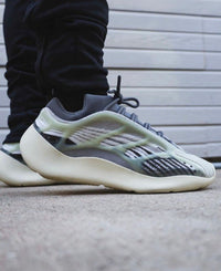 Close-up zijaanzicht van Yeezy 700 V3 Fade Salt aan voet met zwarte broek, focus op zoolcurve en organisch cage design