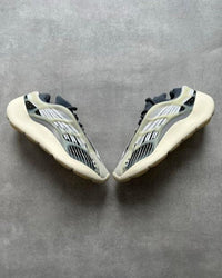 Flatlay van twee Yeezy 700 V3 Fade Salt sneakers op betonnen ondergrond, met zicht op futuristische cage en vetersysteem