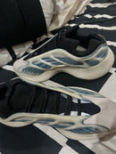 Top view van de Adidas Yeezy Kyanite on feet, vastgelegd boven zwart-wit beddengoed met focus op de glow cage en zoolconstructie