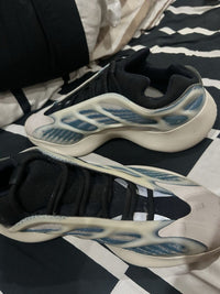 Top view van de Adidas Yeezy Kyanite on feet, vastgelegd boven zwart-wit beddengoed met focus op de glow cage en zoolconstructie