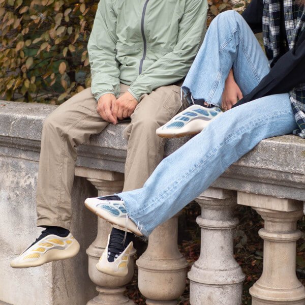 On-foot beeld van de Yeezy 700 Kyanite gedragen met jeans en earth-tone outfit, zittend op balustrade in stadse omgeving