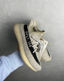 Adidas Yeezy Boost 350 V2 Slate HP7870 vastgehouden, met focus op de contrasterende zwarte zijstreep en doorschijnende zool
