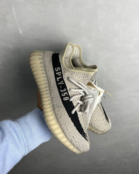 Adidas Yeezy Boost 350 V2 Slate HP7870 vastgehouden, met focus op de contrasterende zwarte zijstreep en doorschijnende zool