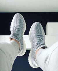 Adidas Yeezy Boost 350 V2 Static EF2905 gedragen met witte broek, waarbij de grijze knit details en reflecterende accenten zichtbaar zijn