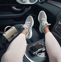 Adidas Yeezy Boost 350 V2 Zebra CP9654 gedragen in een auto-interieur, waarbij de opvallende strepen en rode branding zichtbaar zijn