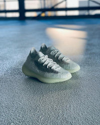 Lifestyle foto van de Yeezy Boost 380 Calcite Glow op betonnen vloer met natuurlijk licht, gefocust op de strakke witte colorway en exclusieve lichtgevende zool