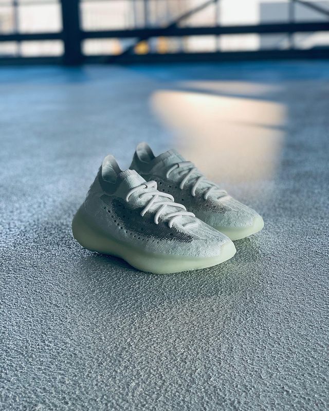 Lifestyle foto van de Yeezy Boost 380 Calcite Glow op betonnen vloer met natuurlijk licht, gefocust op de strakke witte colorway en exclusieve lichtgevende zool