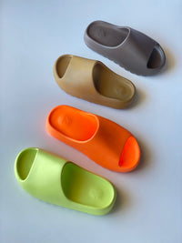 In-hand shot van Yeezy Slide Glow Green GX6138 – neon groene kleur, diepe zool en lichte EVA-constructie onder zonlicht