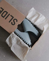 In-hand shot van Yeezy Slide Salt – lichtgewicht feel, diepe zoolribbels en soft grey kleur duidelijk zichtbaar in daglicht