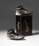 Air Jordan 1 Día De Muertos naast zwarte schoenendoos met gouden accenten – luxe presentatie met thematische illustraties en symboliek