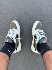 Air Jordan 1 Low OG Travis Scott Medium Olive (SKU DM7866‑200) – in‑hand shot met zicht op reversed Swoosh, Cactus Jack heel-logo en olive rubber outsole