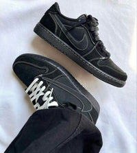 Air Jordan 1 Low OG Travis Scott Black Phantom (SKU DM7866‑001) – in‑hand shot met zicht op reversed Swoosh, witte stitching en bee‑logo op hiel